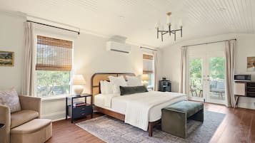 Une chambre dotée d’un grand lit, de tables de chevet, d’une chaise, d’un banc et offrant une vue sur l’extérieur grâce à une porte.