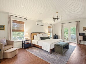 A bedroom with a large bed, bedside tables, a chair, a bench, and a view of the outdoors through a door.