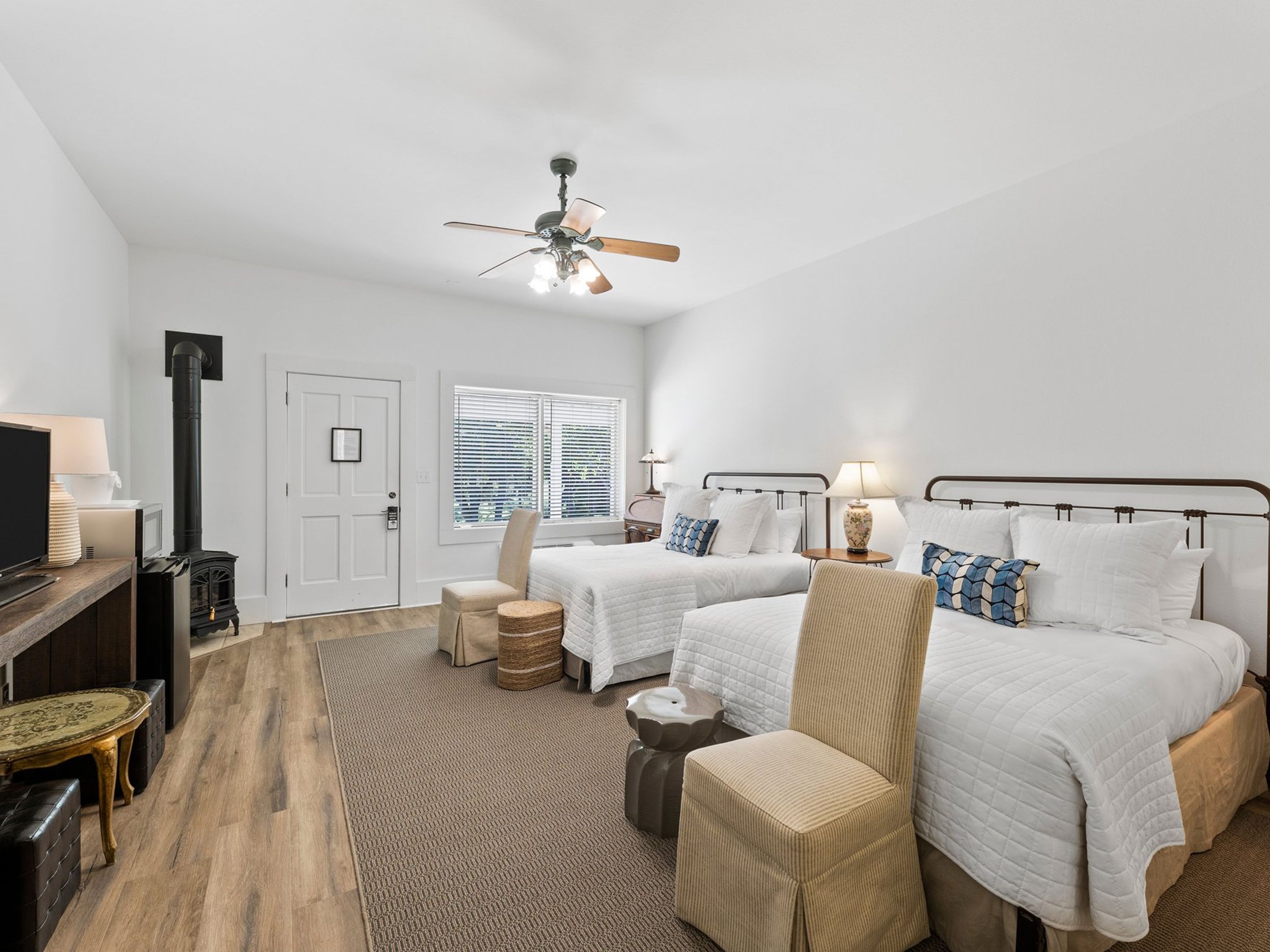 Une chambre d’hôtel avec deux lits, un ventilateur de plafond, une cheminée, une télévision et une fenêtre avec des stores.