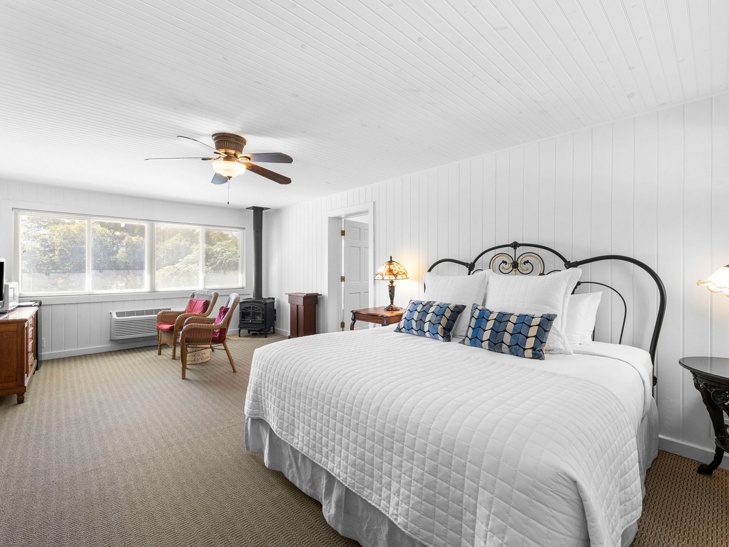 A bedroom with a large bed, a ceiling fan, a heater, a window with blinds, and a chair.
