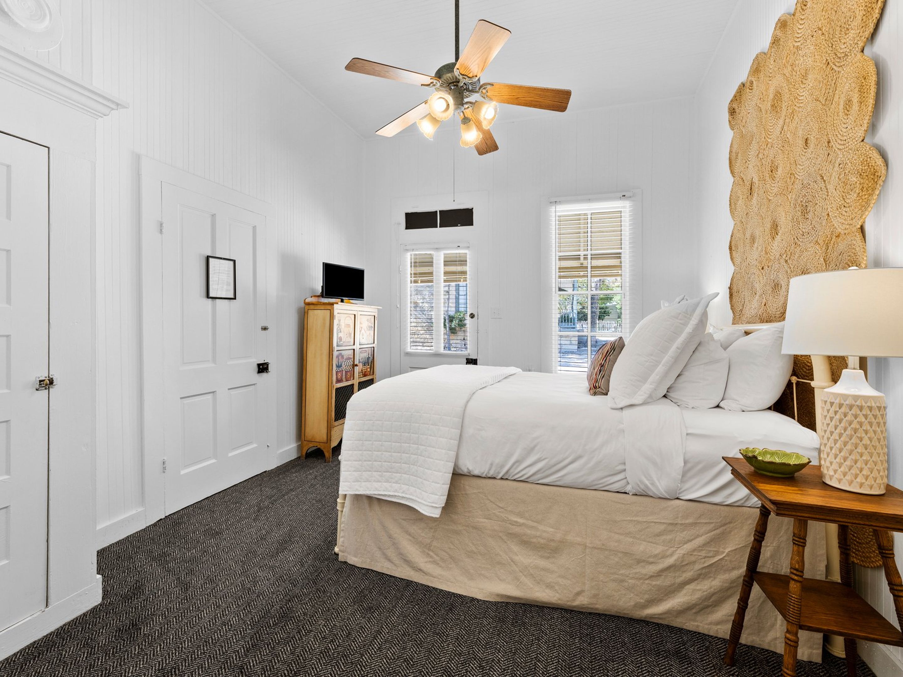 Une chambre à coucher avec un lit, un ventilateur de plafond, une armoire en bois et une fenêtre.