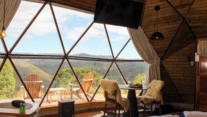 Ein Zimmer mit großem Fenster, Holzmöbeln, einem Fernseher und einem Tisch mit einer Flasche.