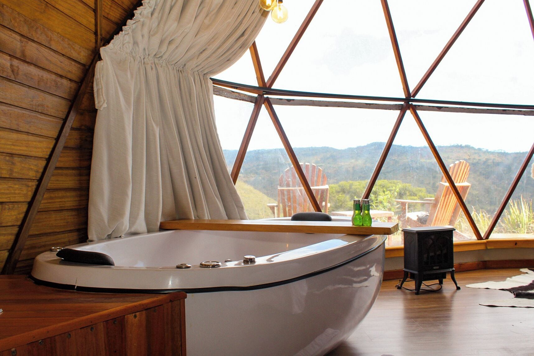 Ein Zimmer mit einer großen Badewanne, Holzwänden, Blick ins Freie und einem mit Vorhängen versehenen Fenster.