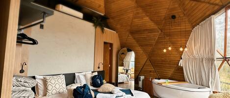 A modern bedroom with a wooden ceiling, a bed, a sitting area with a chair and table, and a view through a window.