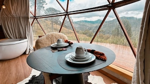 Ein gemütliches Zimmer mit einem großen Fenster, einem runden Tisch mit Tellern und Tassen sowie einem flauschigen Teppich.