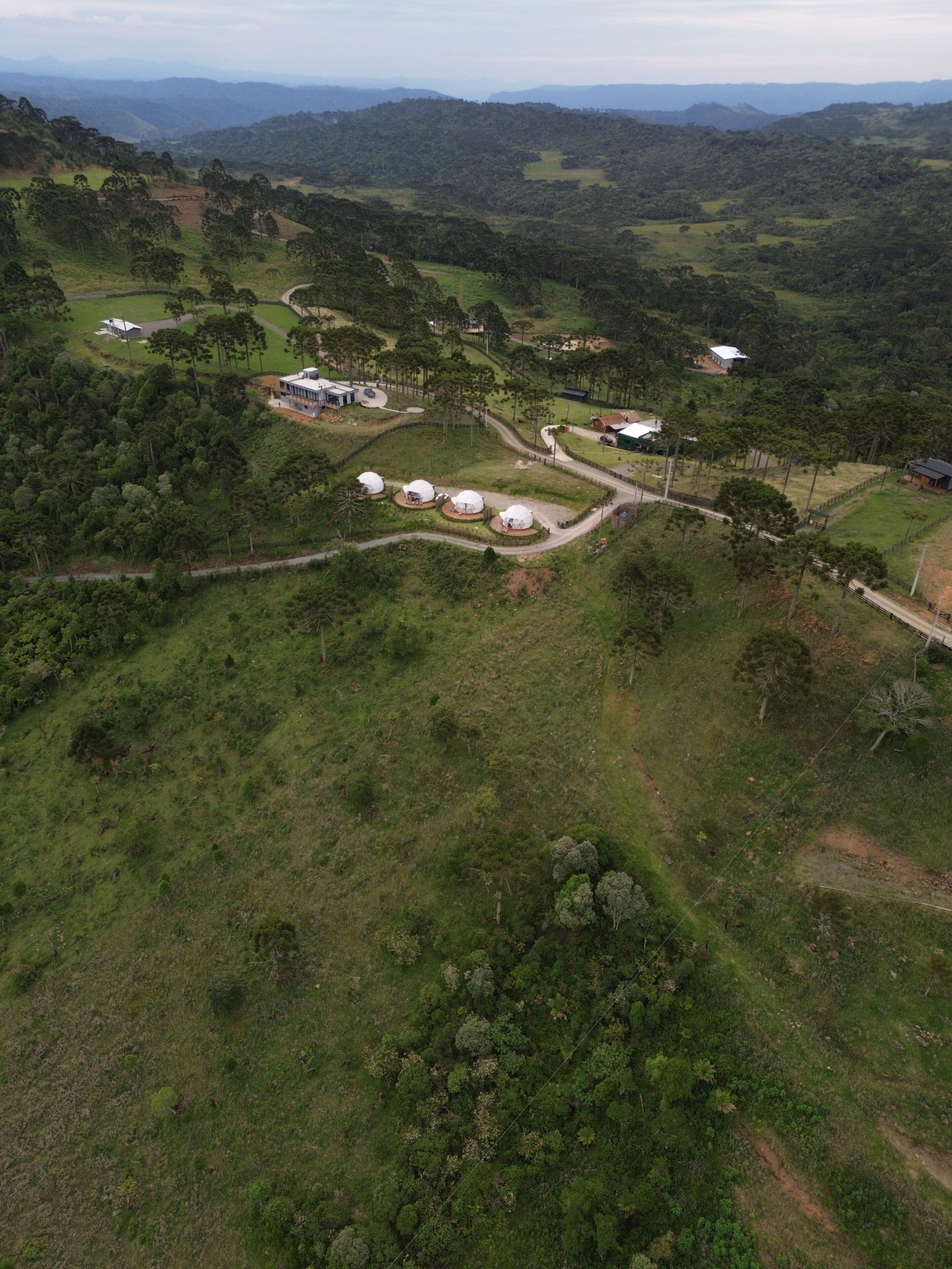 An aerial view of a rural area with several white dome-shaped structures, surrounded by lush greenery and a winding road.