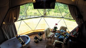 Ein gemütliches Zimmer mit großem Fenster, einer Badewanne, einem Esstisch mit Stühlen und einem Fernseher.