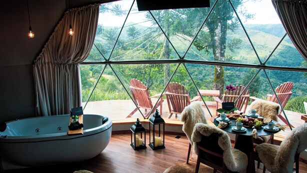 Ein Zimmer mit großem Fenster, Whirlpool, Holzstühlen, einem Esstisch mit Tellern und Kerzen.
