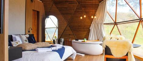 A bedroom with a large bed, a bathtub, and a view through a window.