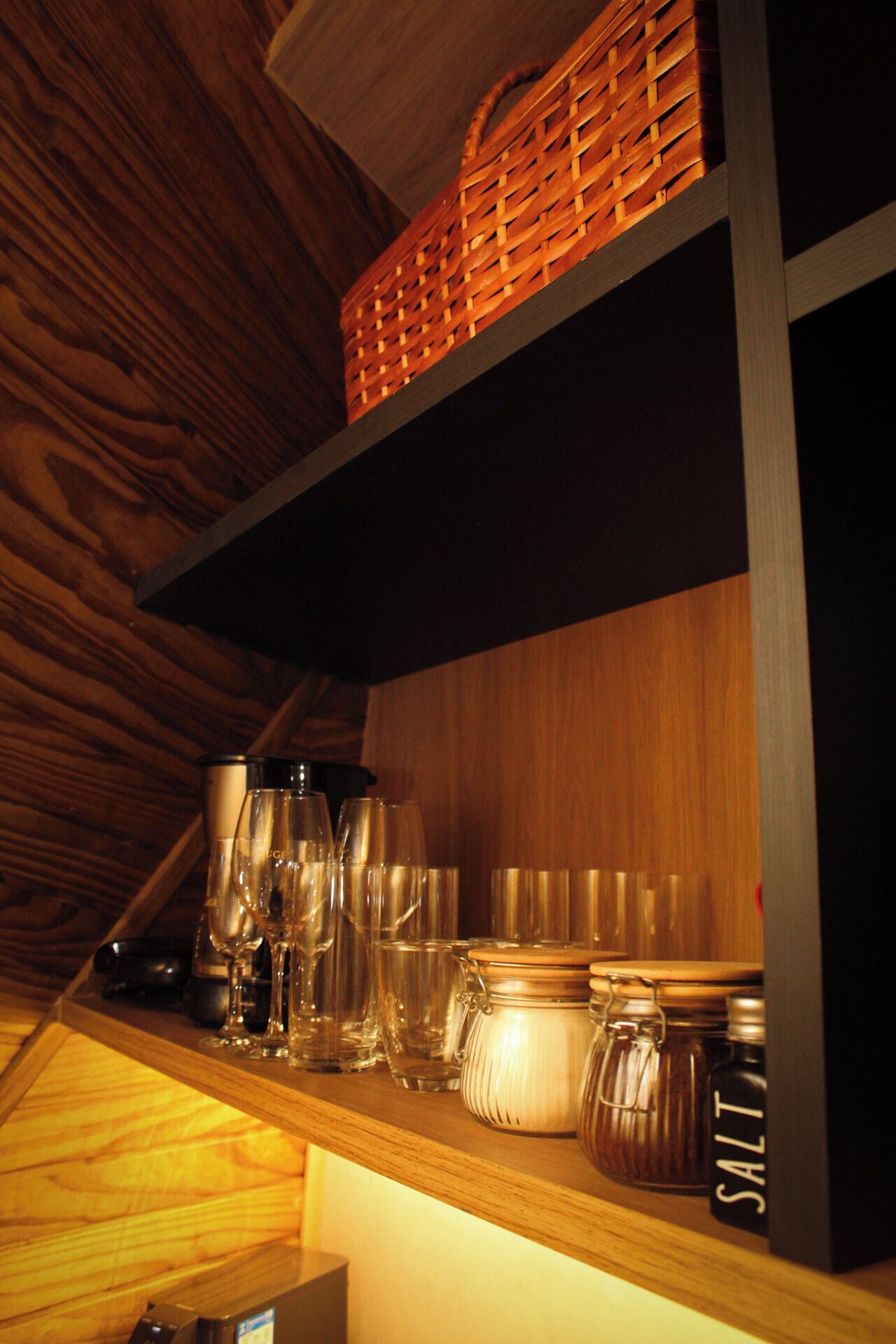 A wooden shelf with glassware and jars.