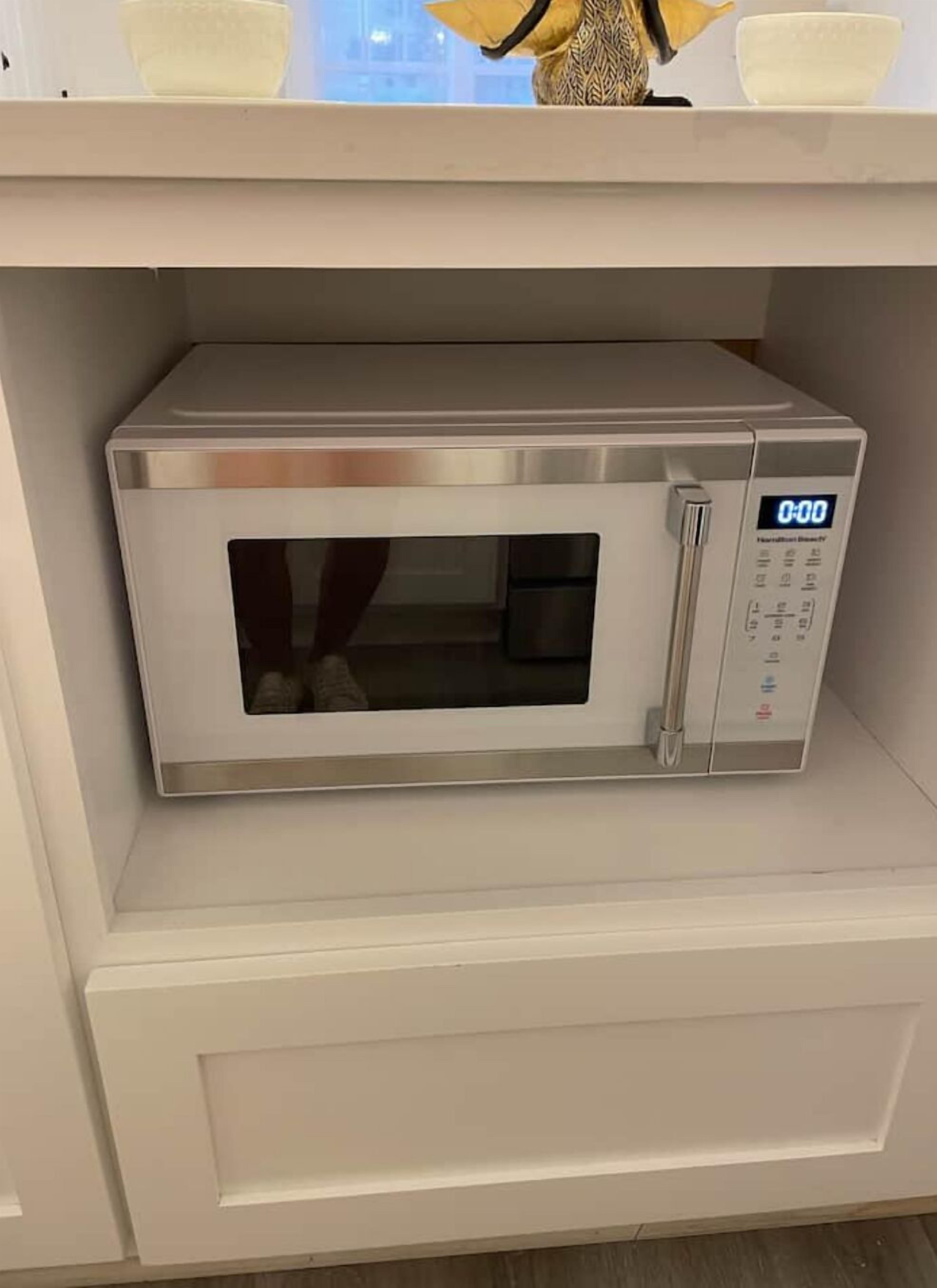 A stainless steel microwave oven with a digital display on a white shelf.