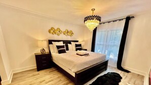 A bedroom with a large bed, a nightstand, a chandelier, and a black furry rug. - Luxury City Loft in Gainesville B (Gainesville)