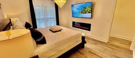 A modern bedroom with a large bed, a TV mounted on the wall, and a chandelier.