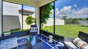 Um alpendre coberto com móveis de vime, uma mesa de vidro e vista para um gramado e um corpo d'água.
