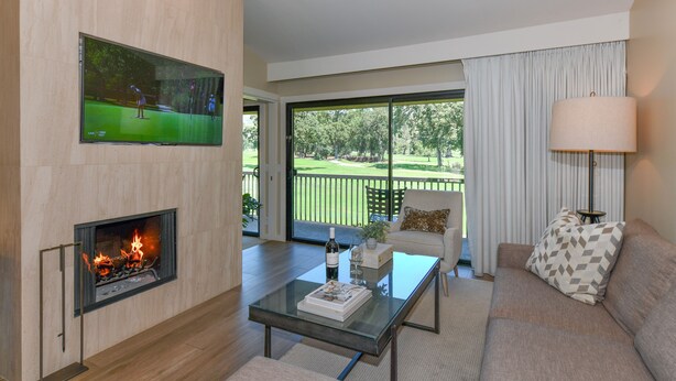 A modern living room with a fireplace, a flat-screen TV, a sofa, a coffee table, and a view of a golf course through large windows. - Napa Golf Course Condo - 2 King Suites + En-Suite Baths - Perfect for 2 couples (Napa)