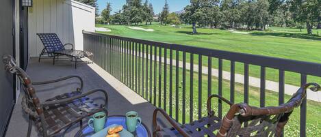 A balcony with wicker chairs, a table with croissants and coffee, and a view of a golf course.