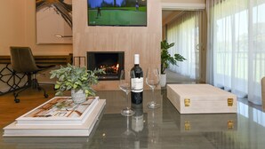 A modern living room with a flat-screen TV displaying a golf game, a fireplace, a table with a bottle of wine, glasses, and a decorative plant. - Napa Golf Course Condo - 2 King Suites + En-Suite Baths - Perfect for 2 couples (Napa)