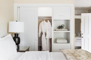 A hotel room with a bed, a bedside table with a lamp, a wardrobe with hanging robes, and a shelf with toiletries. - Napa Golf Course Condo - 2 King Suites + En-Suite Baths - Perfect for 2 couples (Napa)