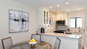A modern kitchen with white cabinetry, a central island, and a dining area with a glass table. - Napa Golf Course Condo - 2 King Suites + En-Suite Baths - Perfect for 2 couples (Napa)