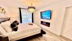A modern bedroom with a large bed, a chandelier, a TV mounted on the wall, and a view of the outdoors through the window. - Luxury City Loft in Gainesville D (Gainesville)