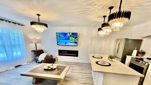 A modern kitchen and living area with a large island, a flat-screen TV, and a chandelier. - Luxury City Loft in Gainesville D (Gainesville)