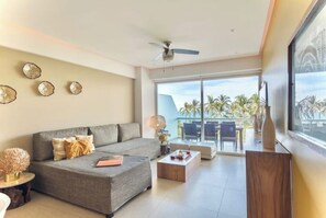 Relax in this stylish living room with a large sofa, coffee table, and side table, offering a view of palm trees and a balcony.