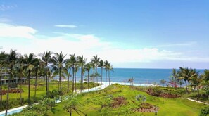 Guests can enjoy a serene ocean view from the resort's beautifully landscaped lawn, surrounded by tropical plants and palm trees.