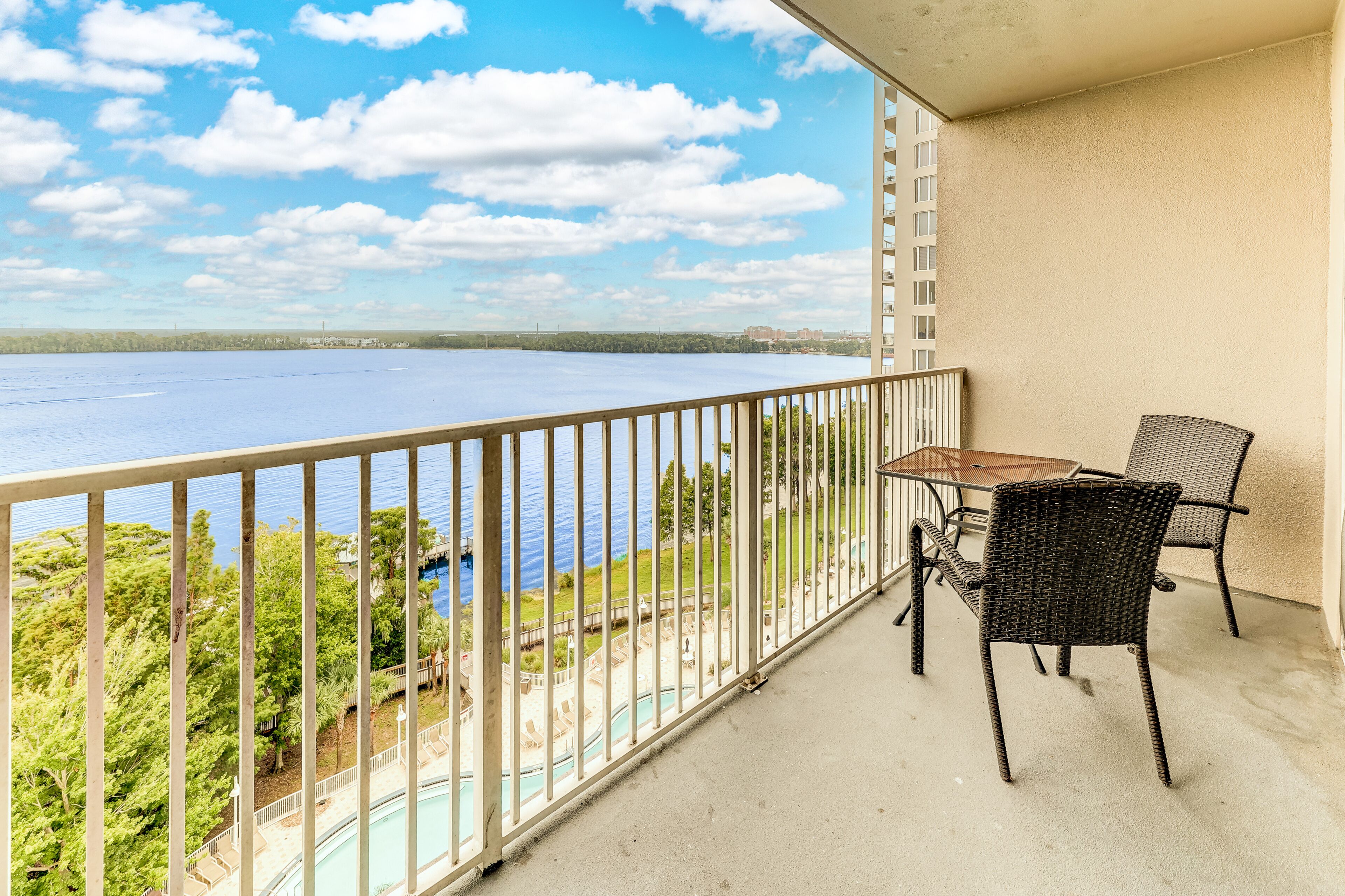 A balcony with a view of a lake, a pool, and a chair.