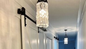 Un pasillo con puertas blancas, suelo de madera y candelabros de cristal colgantes.