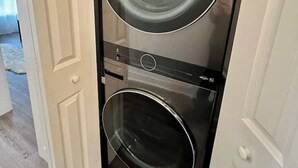 Una unidad compacta de lavadora y secadora con un acabado negro elegante, ubicada en un pasillo estrecho.