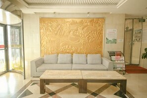 A reception area with a sofa, a coffee table, a wall with a relief sculpture, a glass door, and a poster. - Dingxi Xuxin Hotel (Dingxi)
