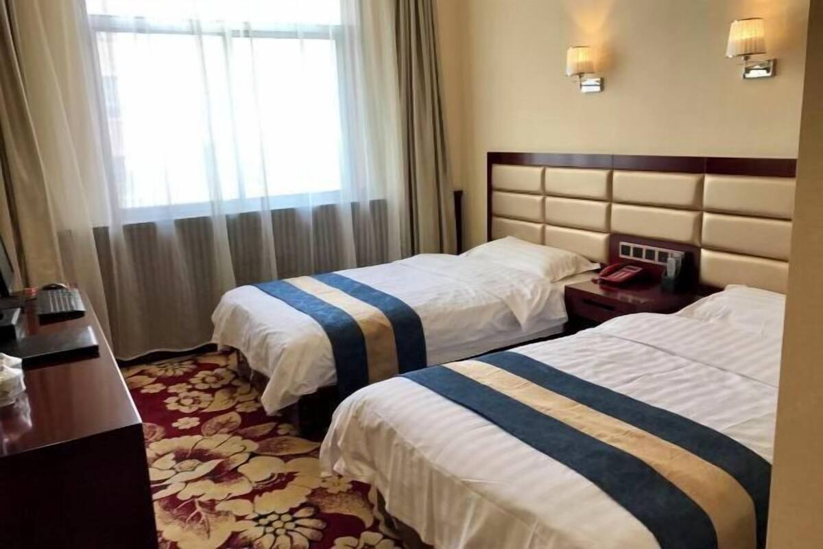 A hotel room with two beds, a desk, and a window with curtains.