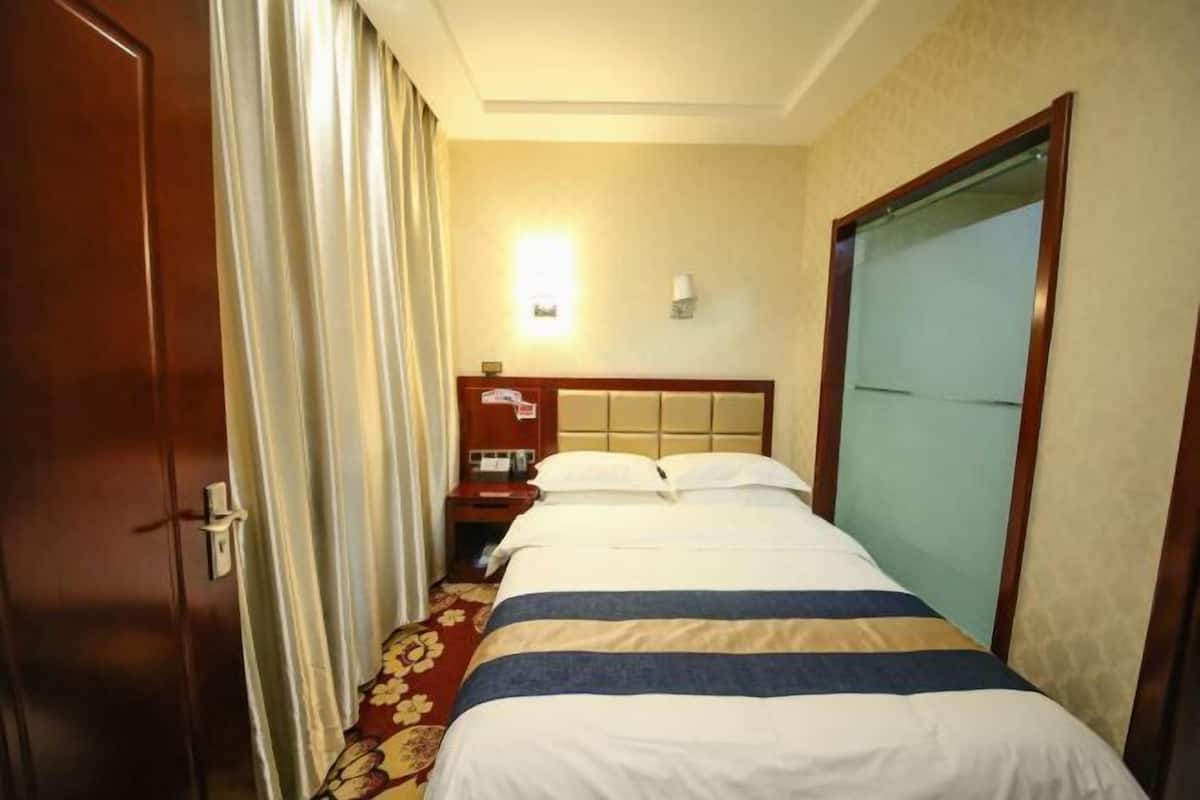 A hotel room with a bed, a nightstand, a lamp, and a window with curtains.