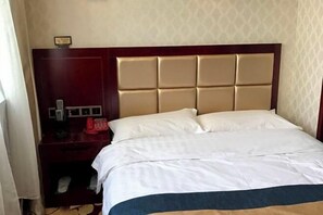 Ein Hotelzimmer mit einem großen Bett, einem hölzernen Kopfteil, einem Nachttisch mit Telefon und einer kleinen Kommode.
