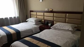 A hotel room with two beds, each with a striped bedspread, a wooden headboard, and bedside lamps.