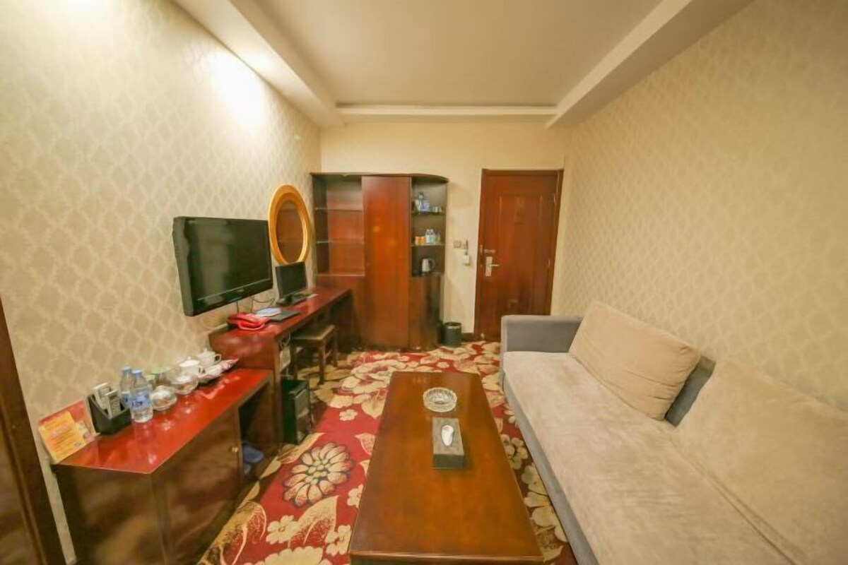 Ein Hotelzimmer mit einer Couch, einem kleinen Tisch, einem an der Wand befestigten Fernseher und einer Holzkommode mit Spiegel.