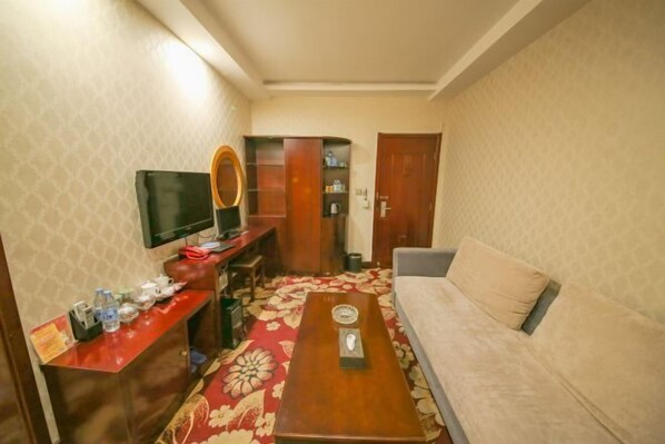 Ein Hotelzimmer mit einer Couch, einem kleinen Tisch, einem an der Wand befestigten Fernseher und einer Holzkommode mit Spiegel.