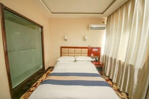 Ein Hotelzimmer mit Bett, Nachttisch, Klimaanlage und einem Fenster mit Vorhängen.