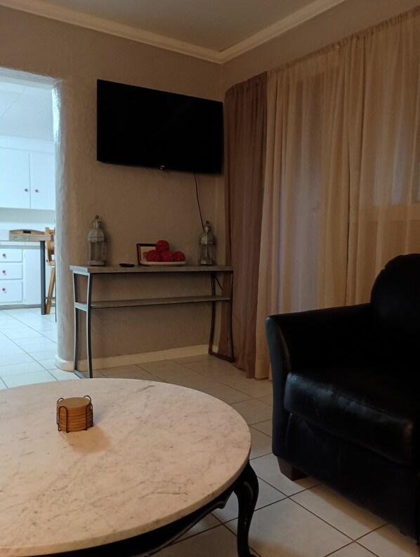 Un salon avec une table ronde, un canapé noir, un téléviseur fixé au mur et un bureau agrémenté d’objets décoratifs.