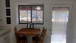 Un petit coin repas avec une table et des chaises en bois, une fenêtre donnant sur l’extérieur et une porte dotée d’un panneau en verre dépoli.