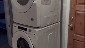 Une machine à laver et un sèche-linge superposés dans une pièce dotée d’une porte en bois et d’un revêtement de sol carrelé.