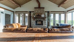 A spacious living room with a stone fireplace, leather sofas, and large windows offering a view of the outdoors.