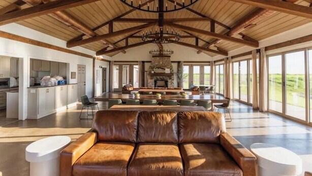 A spacious living area with a large leather sofa, a fireplace, and a high ceiling with exposed beams.