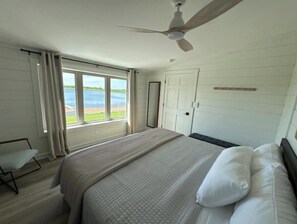 A bedroom with a bed, a ceiling fan, a window with a view of a lake, and a door.