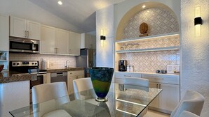 A modern kitchen with white cabinets, a glass dining table, and a decorative bowl centerpiece. - Remodeled 2025 Beachfront Escape – Pool, Views & Walkability (Cabo San Lucas)