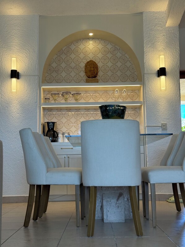 Een moderne eetruimte met een witte tafel, twee stoelen en een decoratieve wand met een centraal geplaatste sculptuur.