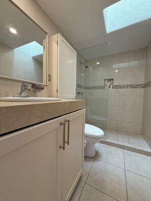 Een badkamer met een wastafel, spiegel, kastje, toilet, douche en betegelde wanden.