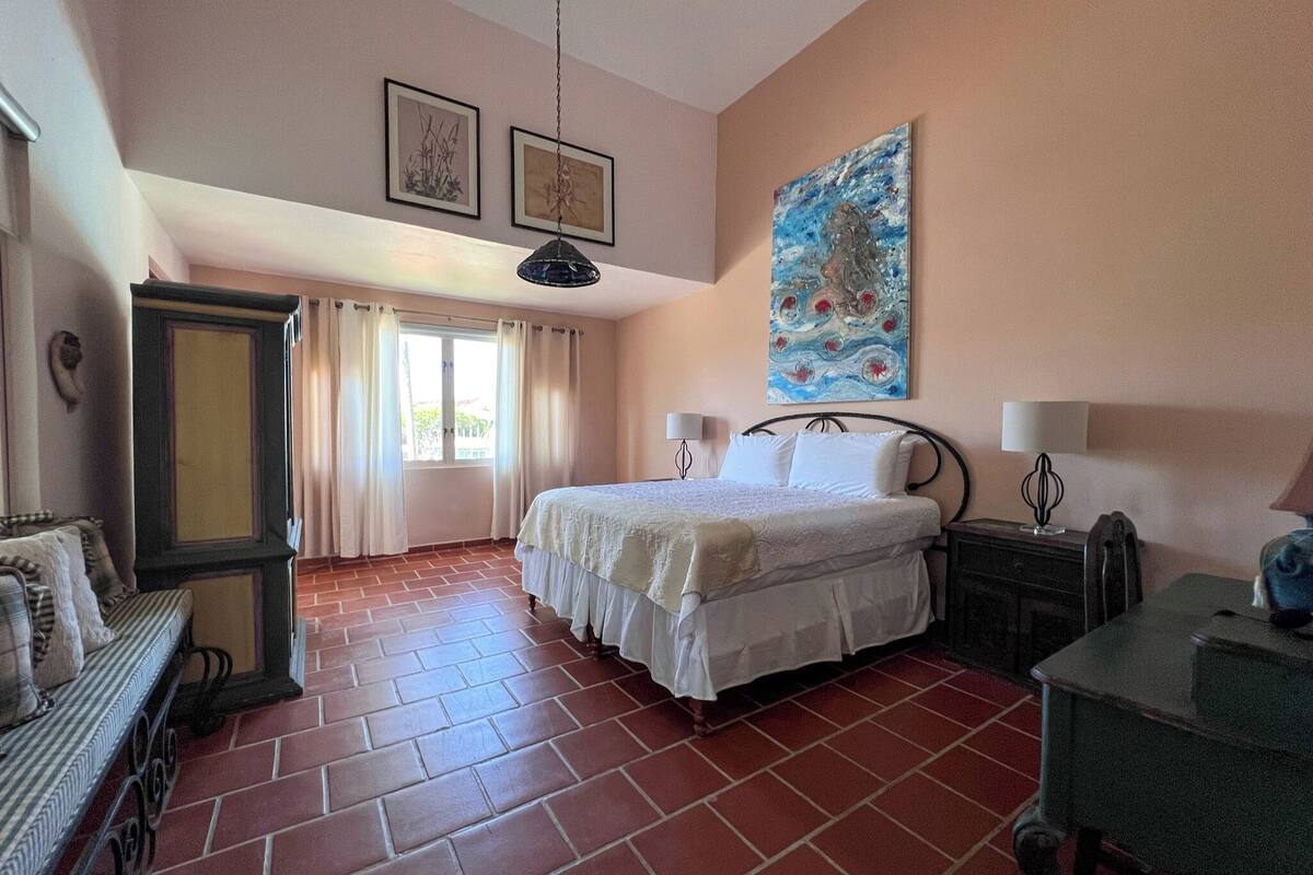 A bedroom with a bed, a nightstand, a desk, a chair, a wardrobe, and a window with curtains.