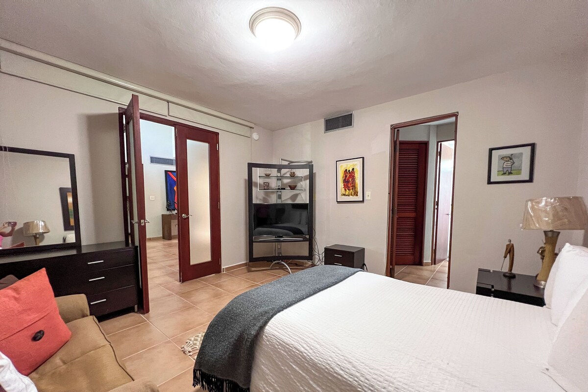 A bedroom with a bed, a dresser, a mirror, a wardrobe, and a desk with a lamp.