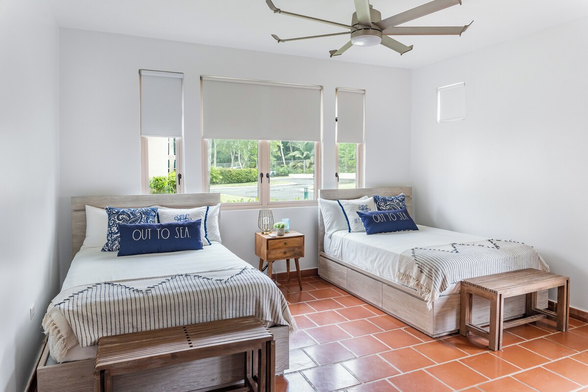 A bedroom with two beds, a ceiling fan, and a view of the outdoors.